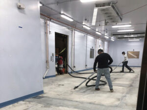 Workers applying epoxy floor coating to a floor. How to Avoid Extra Downtime when Applying Epoxy Floor Coatings